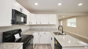 Kitchen featuring light stone countertops, sink, white cabinets, and black appliances