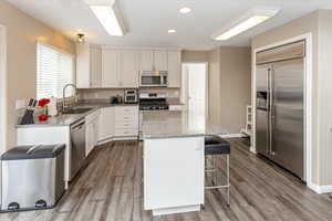 Kitchen featuring updated white cabinets, sink, light stone countertops, appliances with stainless steel finishes, and a kitchen island