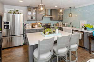 ADU Kitchen featuring a center island, wall chimney range hood, sink, decorative light fixtures, and stainless steel appliances