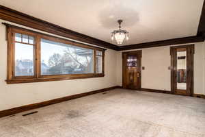 Empty room featuring carpet floors, a notable chandelier, and ornamental molding