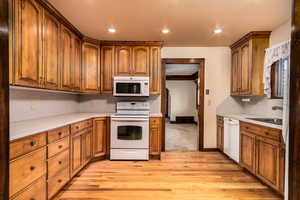 Kitchen featuring light wood-type flooring, white appliances, tasteful backsplash, and sink