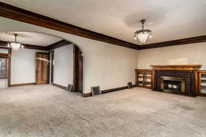 Unfurnished living room with carpet, ornamental molding, a fireplace, and an inviting chandelier