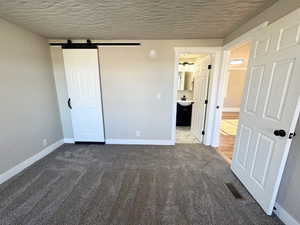 Unfurnished bedroom with dark colored carpet, sink, a barn door, a textured ceiling, and connected bathroom