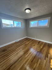 Empty room with a textured ceiling, hardwood / wood-style floors, and plenty of natural light