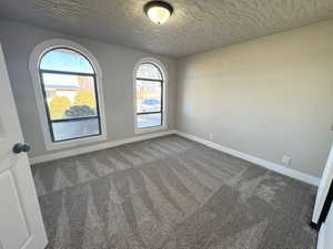 Spare room featuring dark colored carpet and a textured ceiling