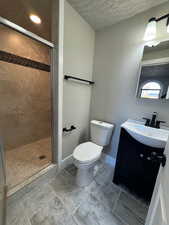 Bathroom with a tile shower, vanity, a textured ceiling, and toilet