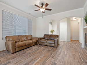 Living room with a tile fireplace, light hardwood / wood-style flooring, ceiling fan, and crown molding