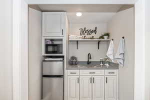 We Bar - kitchen featuring stainless steel mini refrigerator, stainless steel counters, white cabinetry, sink, and black mini microwave