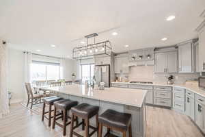 Kitchen featuring light LVP flooring, a breakfast bar, gas stovetop, a kitchen island with sink, and stainless steel refrigerator