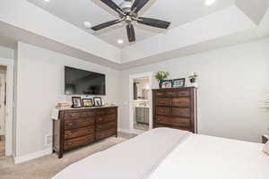 Bedroom with a tray ceiling, ensuite bath, ceiling fan, and carpet