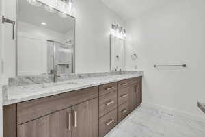 Bathroom featuring marble finish floor, a marble finish shower, double vanity, visible vents, and baseboards