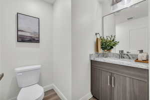 Bathroom with visible vents, toilet, vanity, wood finished floors, and baseboards