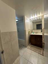 Bathroom with tile patterned floors, vanity, tile walls, and tiled shower / bath