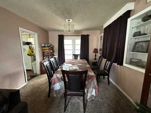 Carpeted dining room featuring a textured ceiling and a chandelier