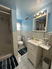 Bathroom with tile patterned floors, walk in shower, vanity, tile walls, and toilet