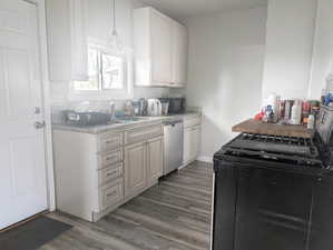 Kitchen featuring black appliances, white cabinets, hanging light fixtures, light stone countertops, and dark hardwood / wood-style flooring