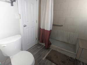 Bathroom with a shower with curtain, hardwood / wood-style floors, and toilet