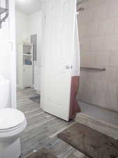 Bathroom featuring hardwood / wood-style flooring, a shower with curtain, toilet, and electric panel