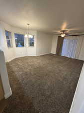 Carpeted spare room featuring ceiling fan with notable chandelier and a textured ceiling