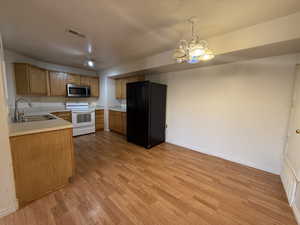 Kitchen with a notable chandelier, black fridge with ice dispenser, white electric range, hanging light fixtures, and sink