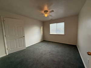 Carpeted empty room with ceiling fan and a textured ceiling