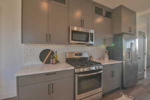 Model Home picKitchen featuring backsplash, gray cabinetry, stainless steel appliances, and dark hardwood / wood-style floors