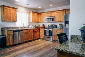 Kitchen featuring dark hardwood / wood-style flooring, sink, stone countertops, and appliances with stainless steel finishes