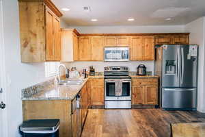 Kitchen featuring light stone countertops, sink, appliances with stainless steel finishes, and dark wood-type flooring