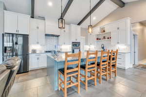 Kitchen with vaulted ceiling with beams, white cabinetry, hanging light fixtures, and appliances with stainless steel finishes