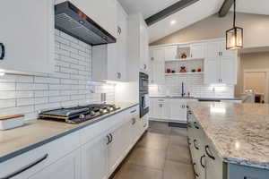 Kitchen featuring wall chimney exhaust hood, stainless steel appliances, sink, lofted ceiling with beams, and white cabinets