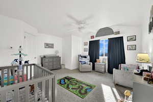 Carpeted bedroom with vaulted ceiling, a nursery area, and ceiling fan