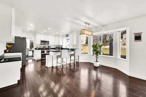 Kitchen featuring stainless steel appliances, white cabinetry, a kitchen island, hanging light fixtures, and a breakfast bar area