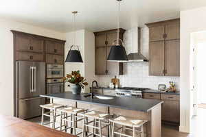 Kitchen with wall chimney exhaust hood, sink, stainless steel appliances, and an island with sink