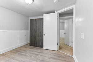 Unfurnished bedroom with a textured ceiling, light hardwood / wood-style floors, and a closet