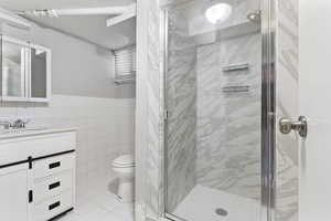 Bathroom featuring vanity, a shower with door, toilet, and tile walls