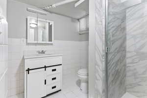 Bathroom featuring vanity, tile patterned floors, toilet, tile walls, and walk in shower