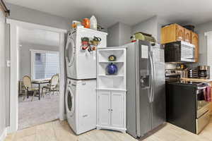 Kitchen with light brown cabinetry, light colored carpet, stacked washer / drying machine, and appliances with stainless steel finishes