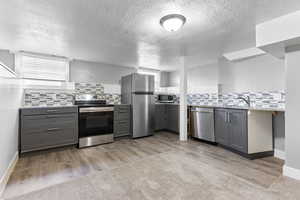 Kitchen featuring gray cabinetry, decorative backsplash, light stone counters, and stainless steel appliances