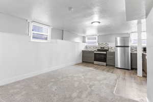 Kitchen with light hardwood / wood-style flooring, decorative backsplash, gray cabinets, a textured ceiling, and stainless steel appliances