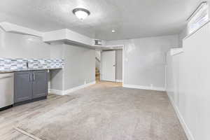 Basement featuring sink, a textured ceiling, and light carpet