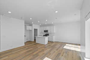 Kitchen featuring white cabinetry, sink, light hardwood / wood-style floors, a kitchen island with sink, and appliances with stainless steel finishes