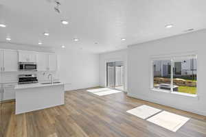 Kitchen with white cabinetry, sink, stainless steel appliances, an island with sink, and light wood-type flooring