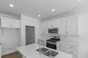 Kitchen with appliances with stainless steel finishes, tasteful backsplash, wood-type flooring, sink, and white cabinets