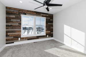 Carpeted empty room featuring ceiling fan and wooden walls