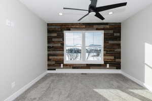 Carpeted spare room featuring ceiling fan and wooden walls