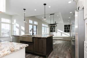 Kitchen with dark brown cabinetry, stainless steel appliances, sink, hanging light fixtures, and an island with sink