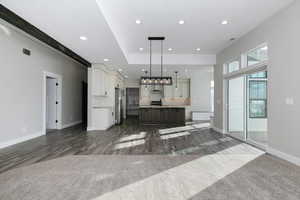 Kitchen with dark colored carpet, pendant lighting, a center island with sink, and stainless steel fridge