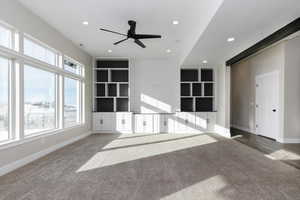 Unfurnished living room featuring carpet flooring, built in features, and ceiling fan