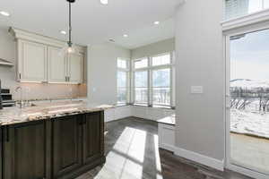 Kitchen with light stone countertops, sink, dark hardwood / wood-style floors, decorative light fixtures, and dark brown cabinets