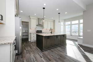 Kitchen featuring wall chimney range hood, light stone counters, dark hardwood / wood-style floors, a kitchen island with sink, and appliances with stainless steel finishes